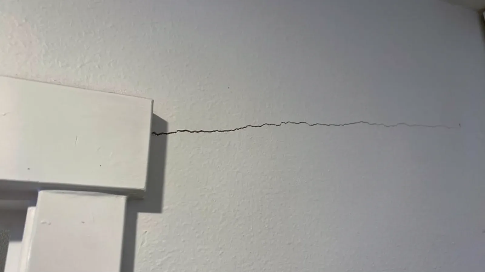 A thin horizontal stress crack running along a painted interior wall from the top corner of a white door casing