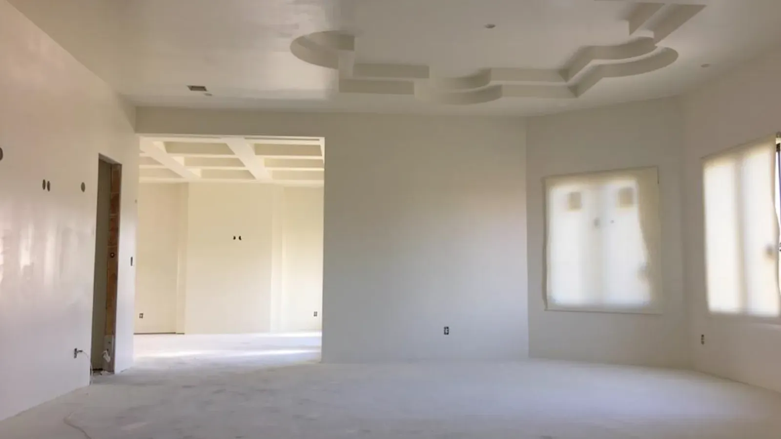 An open interior skim-coated throughout to a smooth uniform finish, with a stepped tray ceiling and plastic-masked windows